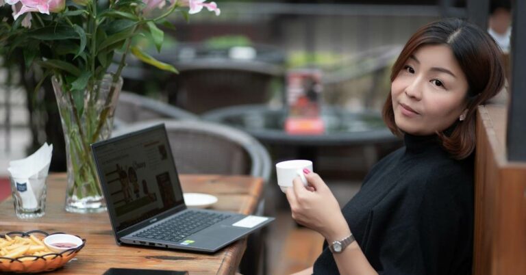 a lady in black holding a white coffee cup sitting at a outdoor cafe
